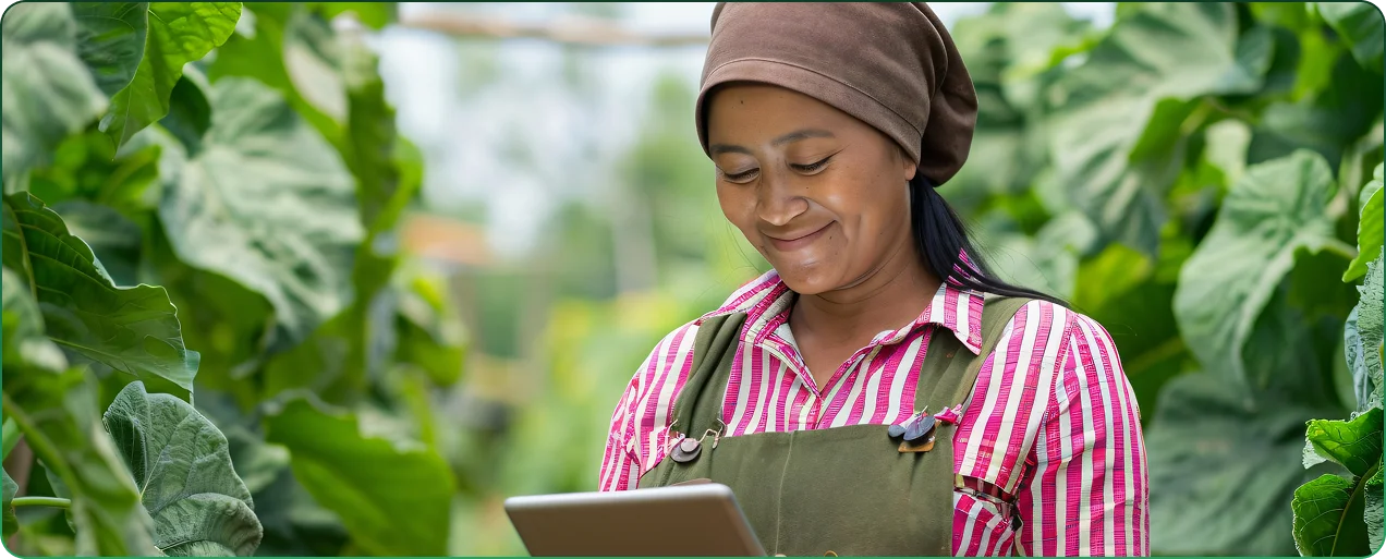 A farm worker smiles while checking a tablet among rows of leafy greenhouse crops